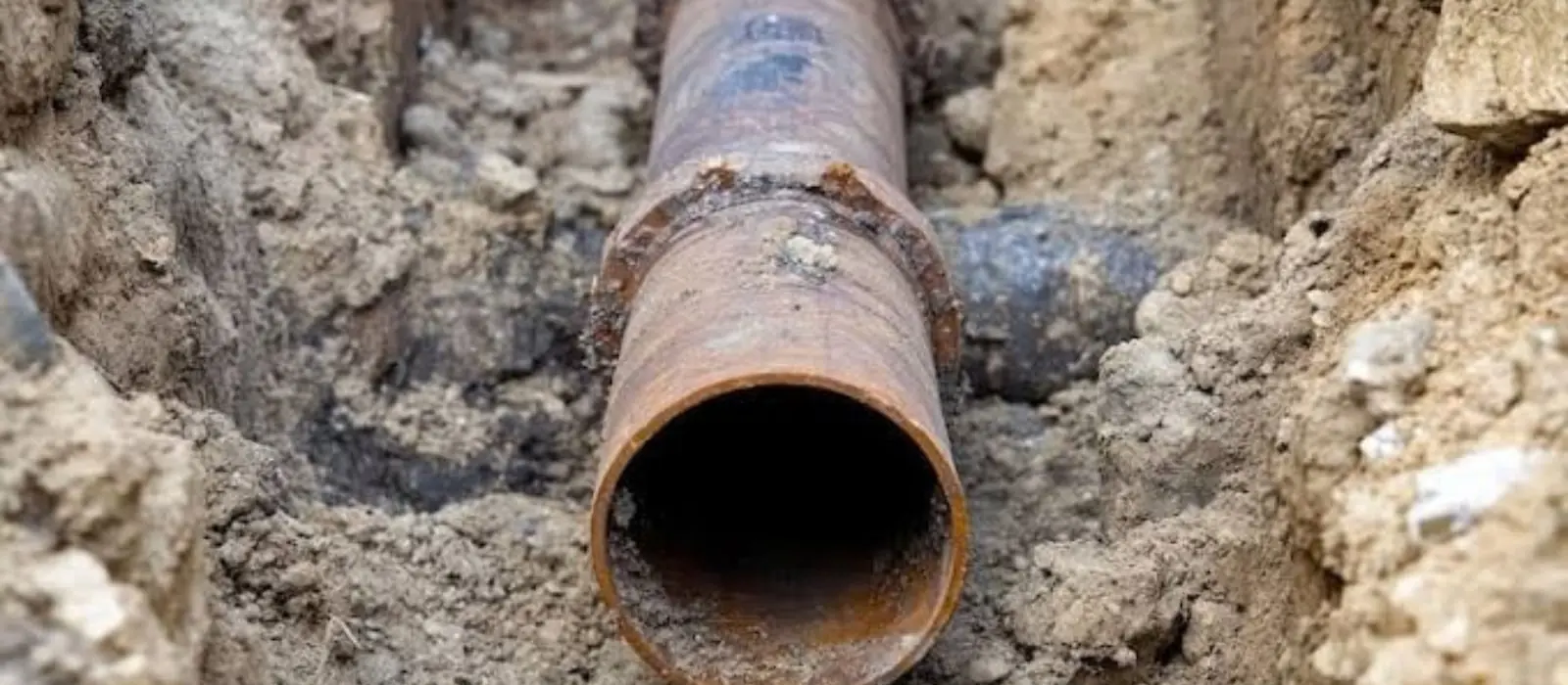 Broken rusted sewer pipe exposed in a dug trench.