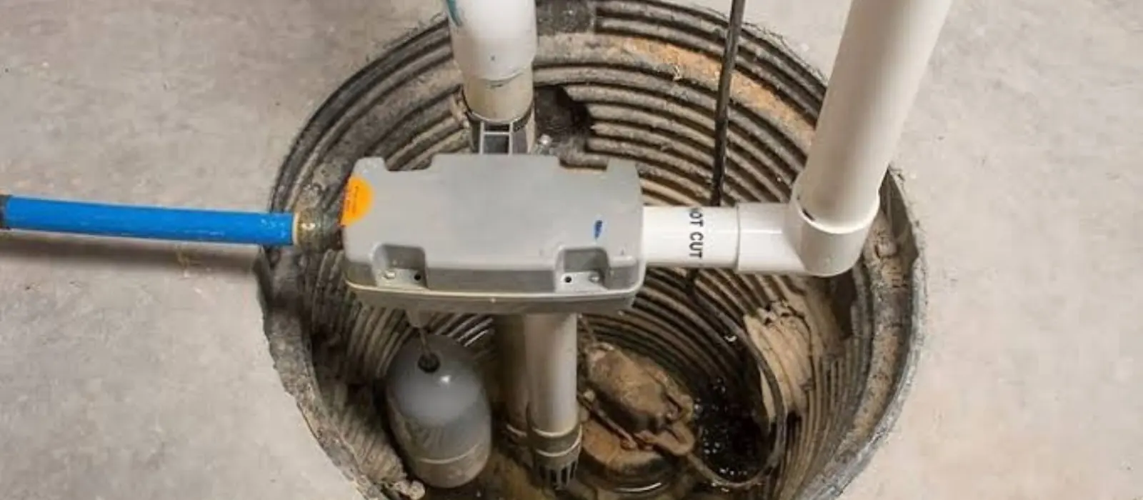 Sump pit with a pump and white discharge pipes set into a basement floor.