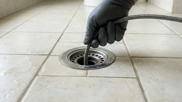 Gloved hand feeding a drain cable into a tiled floor drain.
