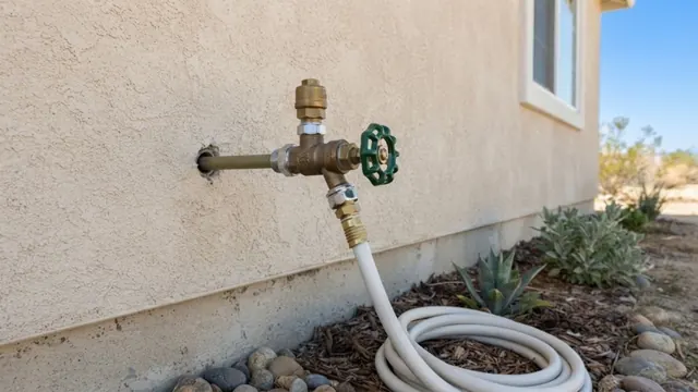 Exterior hose spigot on a house wall with a coiled hose below.