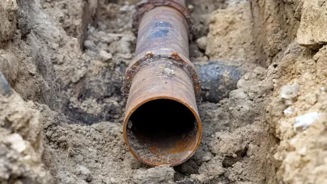 Rusted galvanized steel pipe exposed in a dug trench.