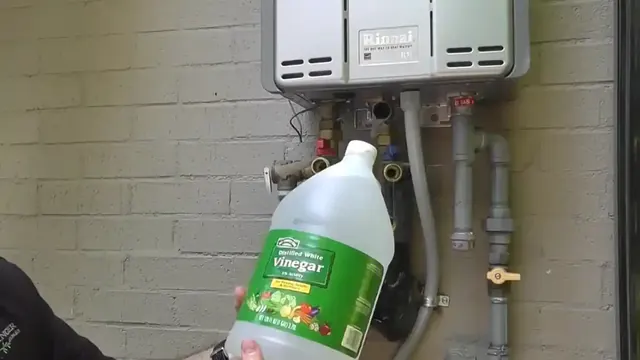 Jug of white vinegar held under a wall-mounted tankless water heater for a descaling flush.
