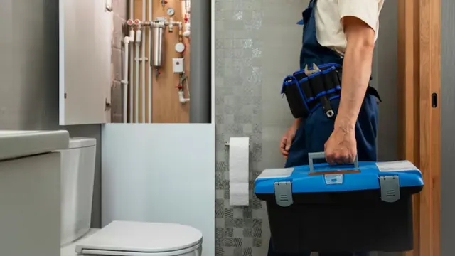 Plumber carrying a toolbox into a bathroom with a toilet.